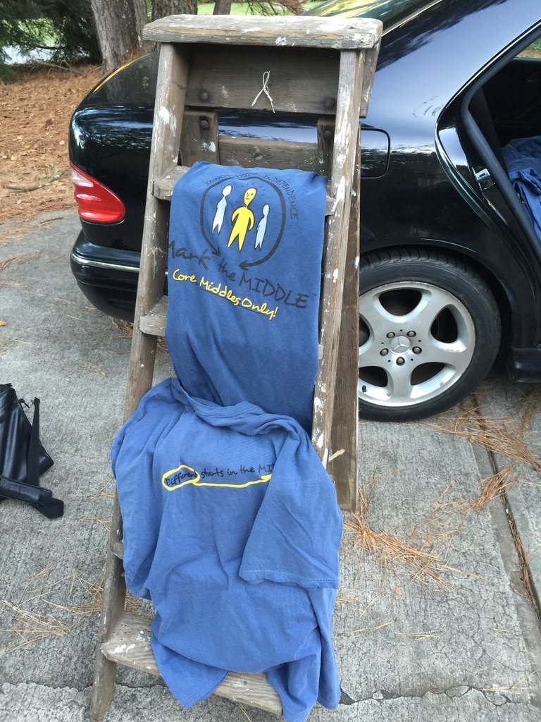 Two blue Mark the Middle shirts on a wooden ladder. One reads Core Middles Only.